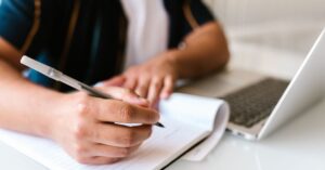 Persona escribiendo en un cuaderno mientras arma su CV
